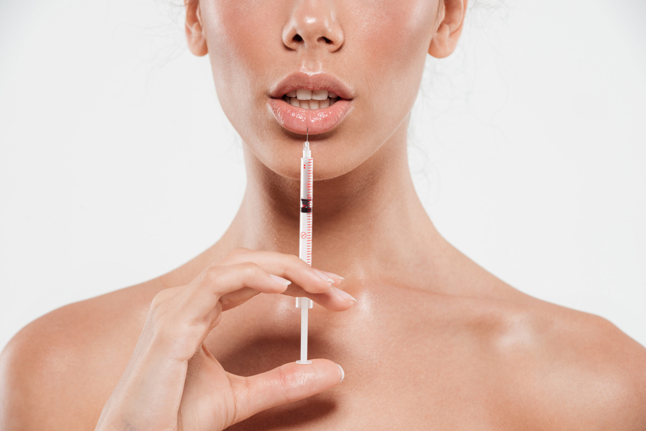 Cropped image of young female face and a hand holding a syringe and making injection in her lip isolated over white background